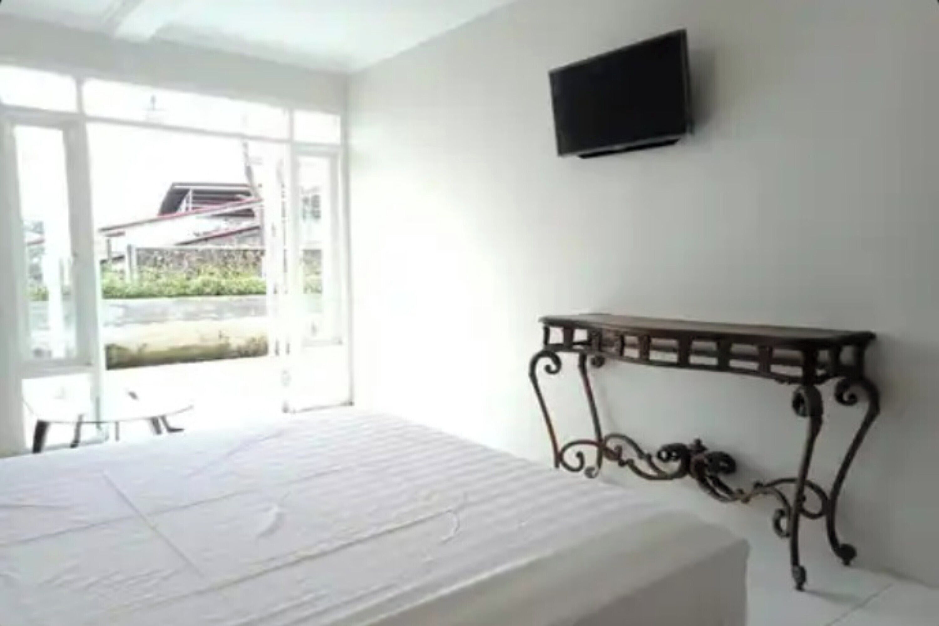 Un dormitorio con cama, televisor montado en la pared y ventana con vistas al exterior.