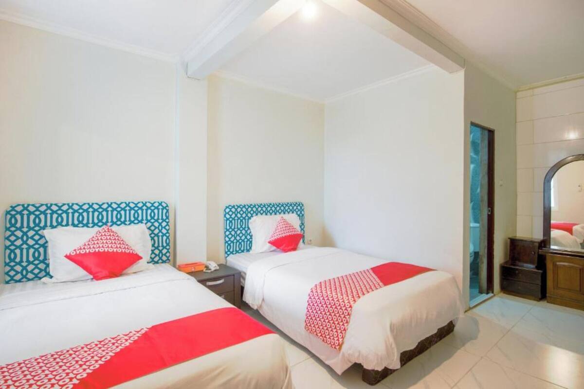 Habitación de hotel con dos camas, cada una con un cabecero estampado, ropa de cama blanca y detalles rojos.