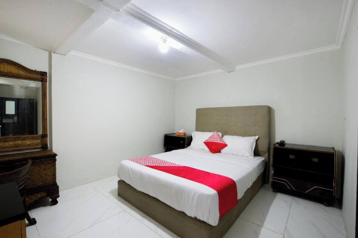 Un dormitorio con una cama, una mesita de noche, un aparador, un espejo y una lámpara en el techo.
