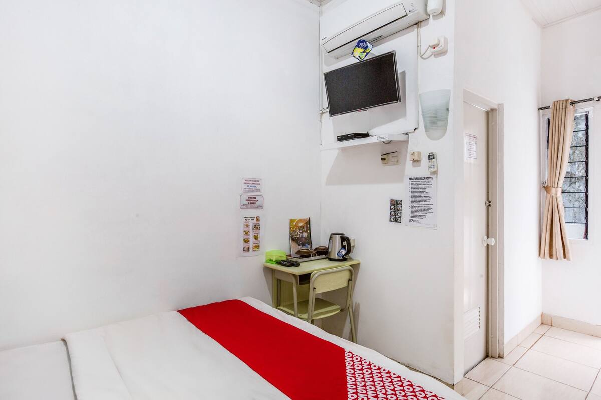 A small hotel room with a bed, a desk, a chair, a TV, and a window with curtains.