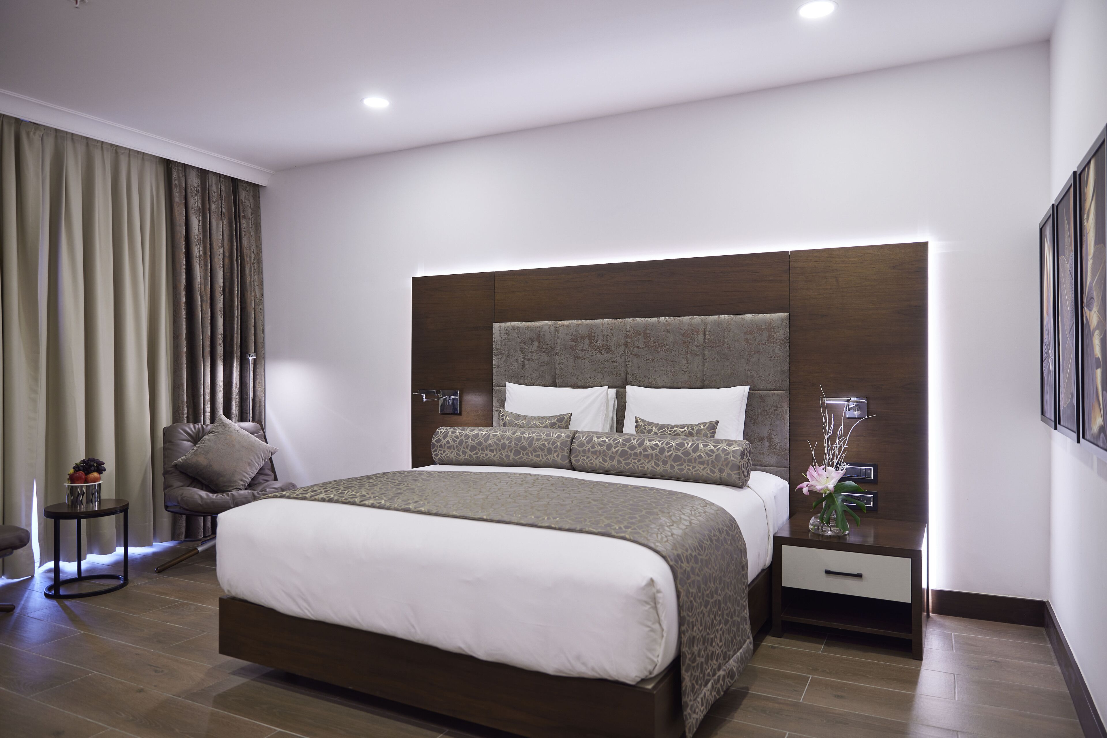 A modern bedroom with a large bed, a nightstand, a chair, and a wall-mounted TV.