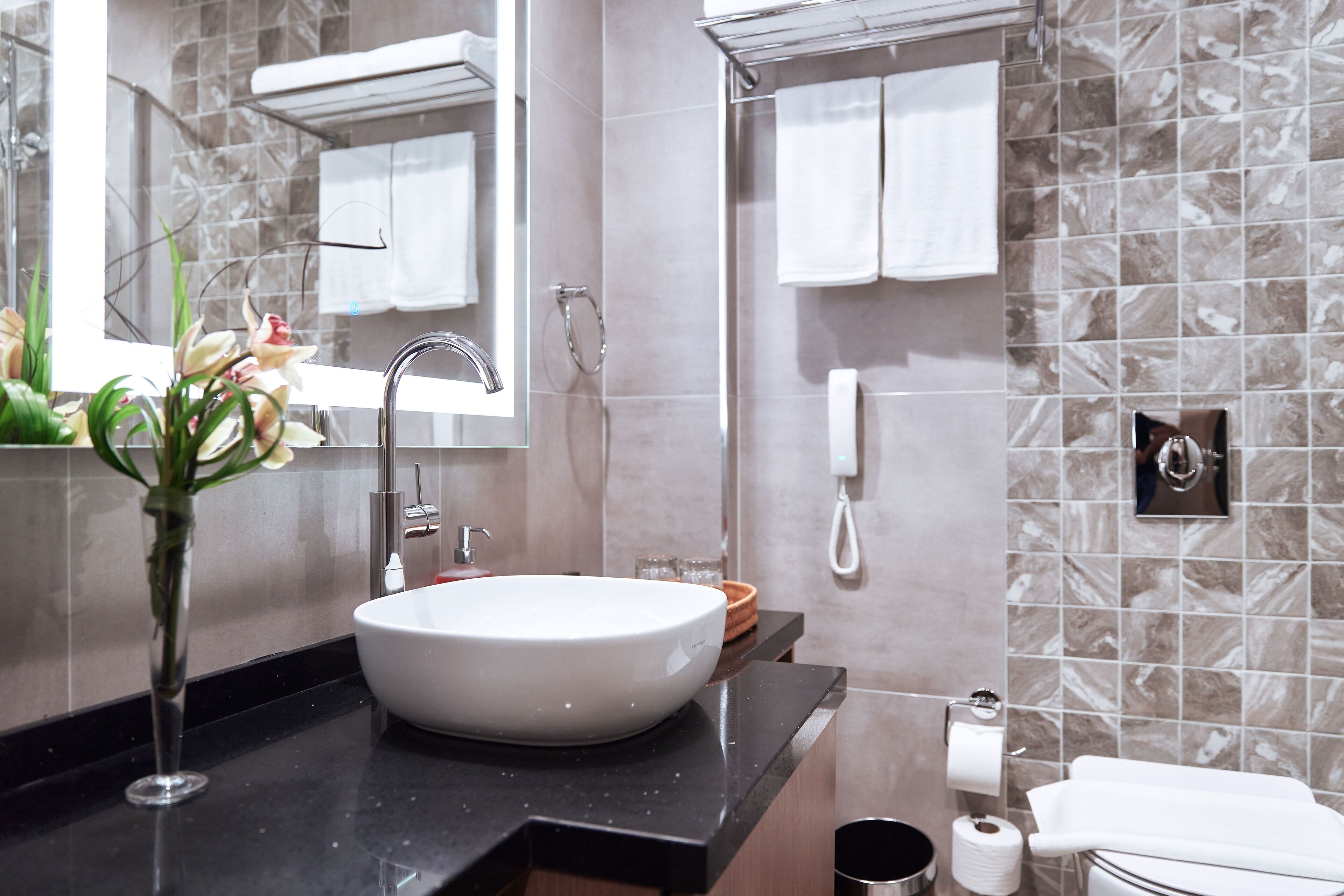 A modern bathroom with a large vessel sink, a handheld showerhead, a towel rack, and a telephone.