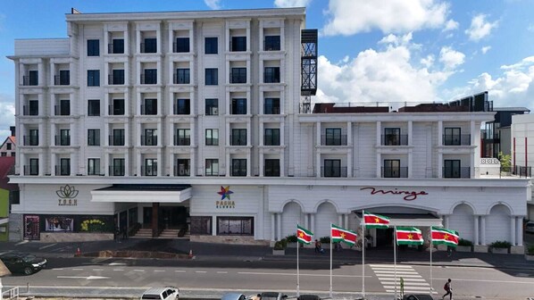 Un hôtel à plusieurs étages, doté d’une façade blanche, d’une entrée principale avec une enseigne et de plusieurs drapeaux exposés à l’extérieur.