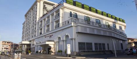 A multi-story hotel with a white facade, green rooftop garden, and a prominent entrance with a statue.