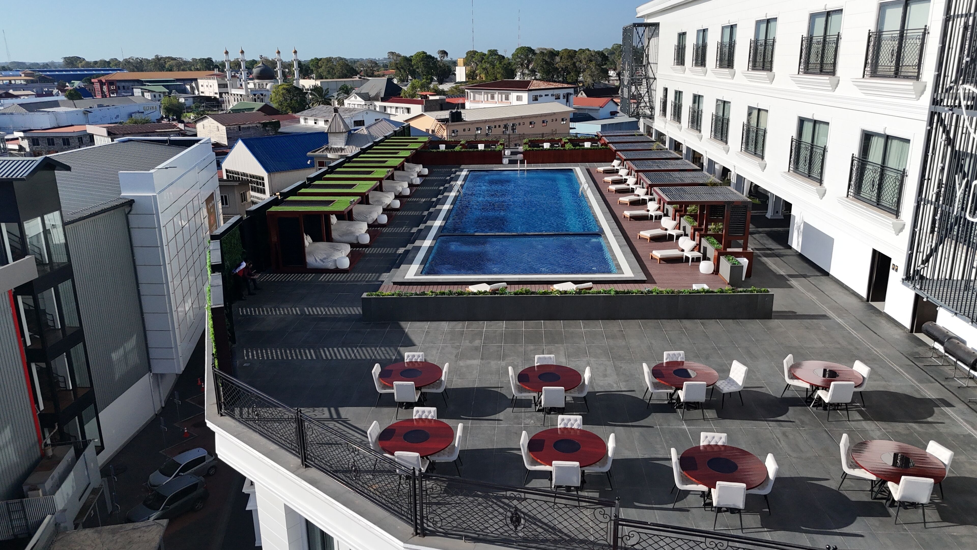 A rooftop pool area with multiple lounge chairs and tables, surrounded by buildings.