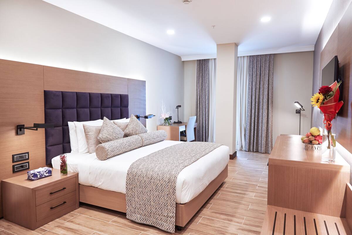A modern hotel room with a large bed, bedside tables, a desk, and a TV mounted on the wall.
