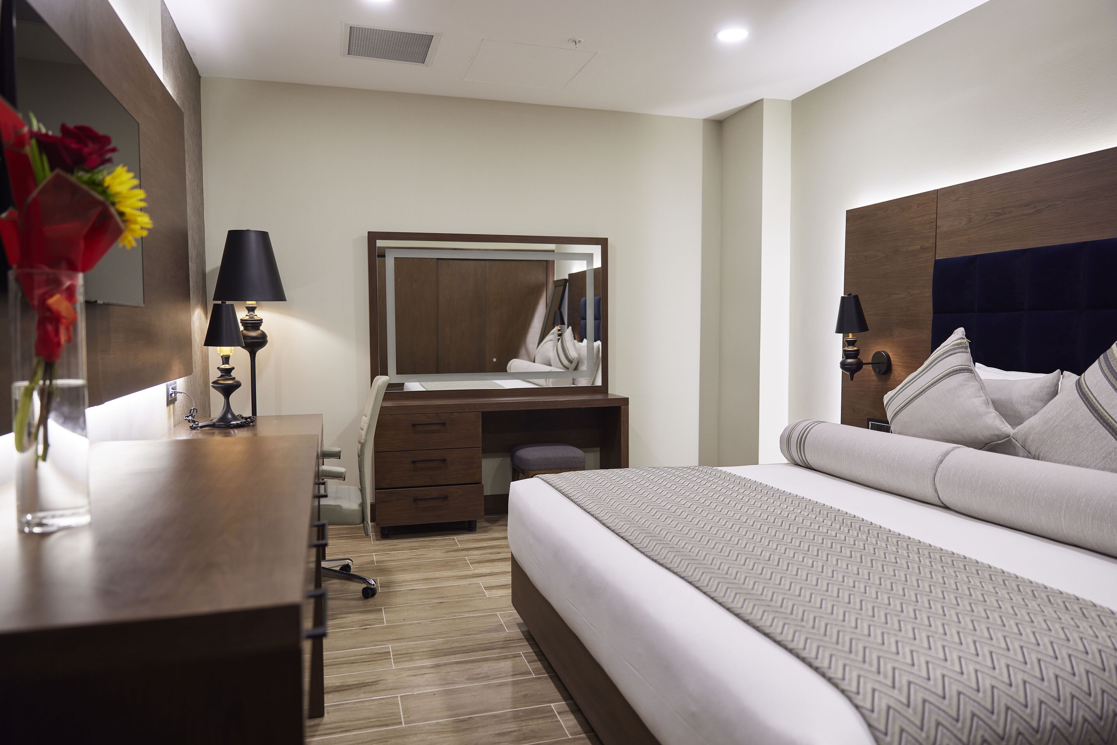 Quarto de hotel moderno com uma cama grande, uma escrivaninha de madeira, um espelho e uma cômoda.