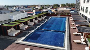 Una piscina en la azotea con varias zonas de descanso, vista de los edificios circundantes y cielo despejado.