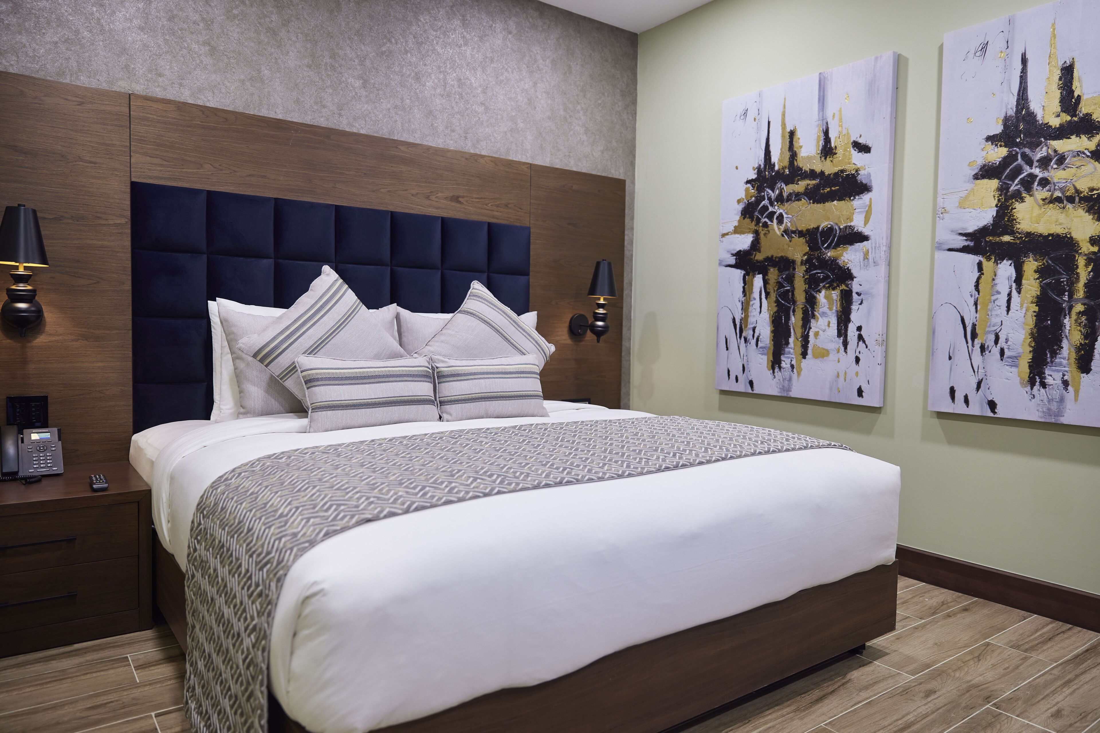A modern hotel room with a large bed, wooden headboard, and two wall-mounted lamps.
