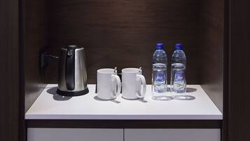 A modern, dark wooden cabinet with a white countertop. On the countertop, there is a silver electric kettle, a white mug, and two water bottles.