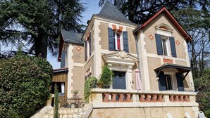 A two-story building with a stone facade, a balcony with lounge chairs, and a staircase leading to the entrance.