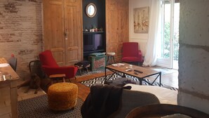A cozy living room with a brick wall, wooden wardrobe, red chairs, a coffee table, and a dog.
