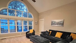 A spacious living room with a large arched window, a sectional sofa with yellow cushions, and a painting on the wall. - Modern Lakefront Retreat - 3br 2ba (Sanford)