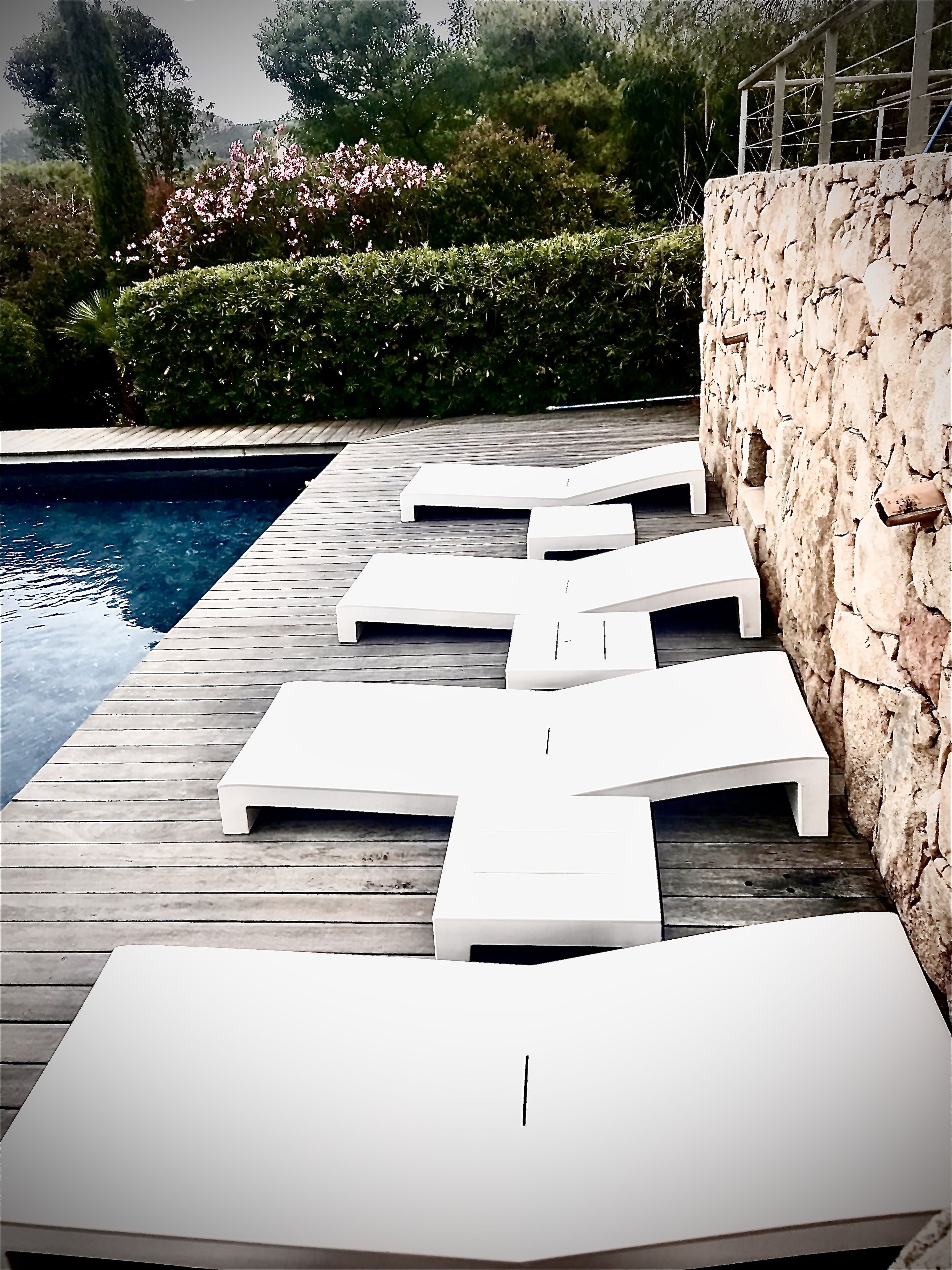 Un área junto a la piscina con sillones blancos y un muro de piedra.