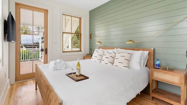 A bedroom with a bed, bedside tables, a TV, and a window with blinds. - Charming 5 Bedroom House - 1 Block to King Street (Charleston)