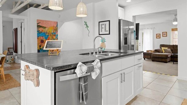 A modern kitchen with a large island, stainless steel appliances, pendant lighting, and a view into the living area. - Secluded Coastal Retreat | Walk to Beach (Cocoa Beach)