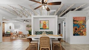 A dining area with a white table, wicker chairs, and a ceiling fan. - Secluded Coastal Retreat | Walk to Beach (Cocoa Beach)