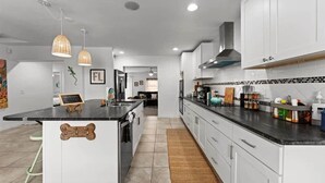 A modern kitchen with white cabinets, a black countertop, and a central island. - Secluded Coastal Retreat | Walk to Beach (Cocoa Beach)
