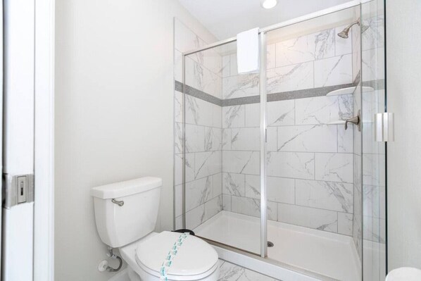 A bathroom with a toilet, a glass-enclosed shower, and marble tiles. - Lakeview 7Br W Pool/ Disney Area (Kissimmee)