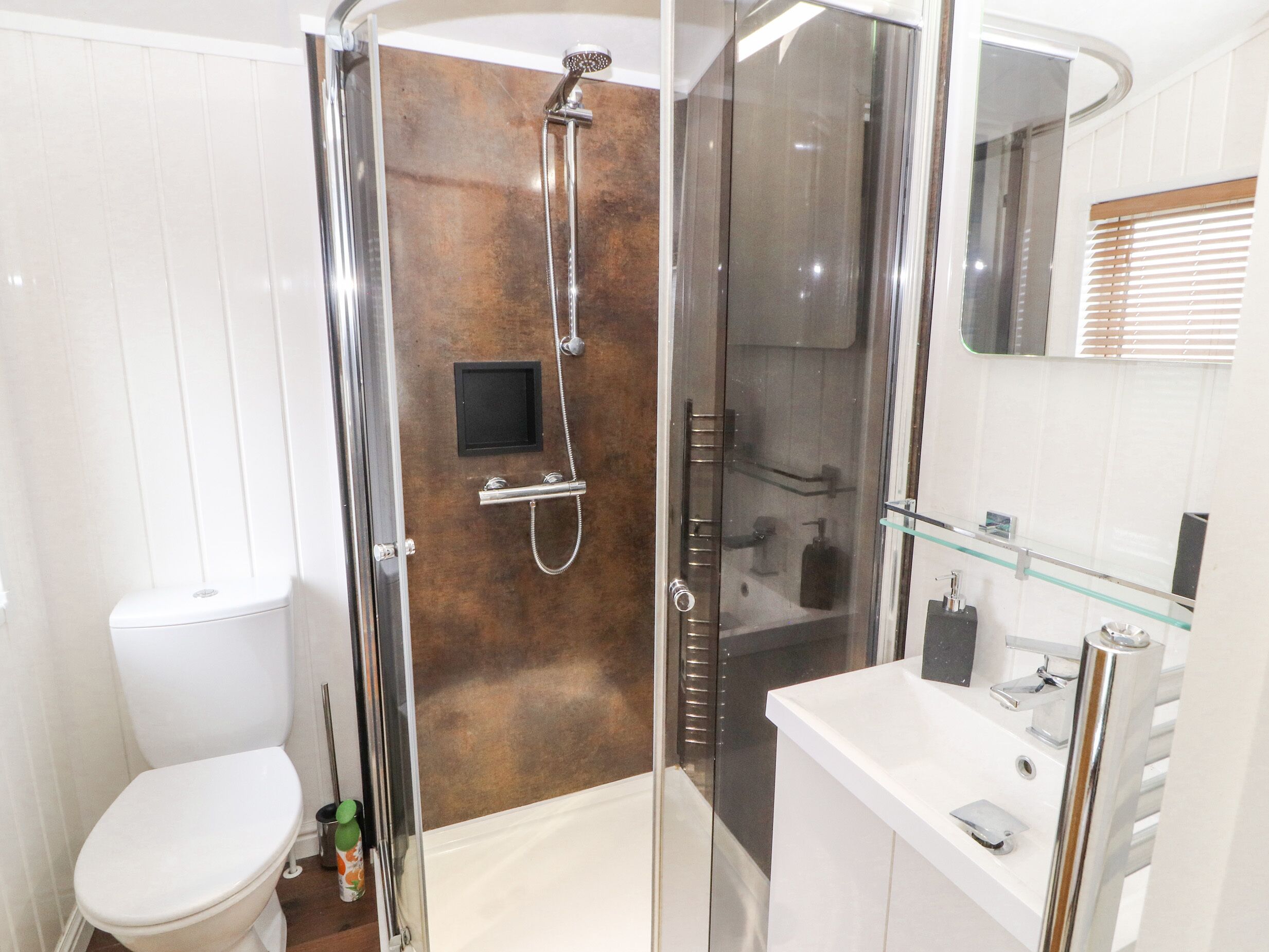 A modern bathroom with a glass-enclosed shower, a white toilet, and a glass-fronted sink with a mirror above.