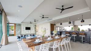 A modern dining area with a long wooden table, white chairs, and ceiling fans. - Spice : 3 Bed Sublime Luxury Five Star Villa (Koh Samui)
