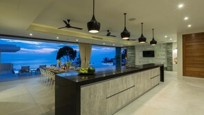 A modern kitchen with a large island, pendant lighting, and a view of the ocean. - Spice : 3 Bed Sublime Luxury Five Star Villa (Koh Samui)