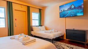 Une chambre d’hôtel avec deux lits, un téléviseur fixé au mur et une porte avec une pancarte rouge.