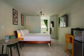 A hotel room with a bed, a desk with a chair, a refrigerator, and a television. - Cozy King Suite (Clearwater)