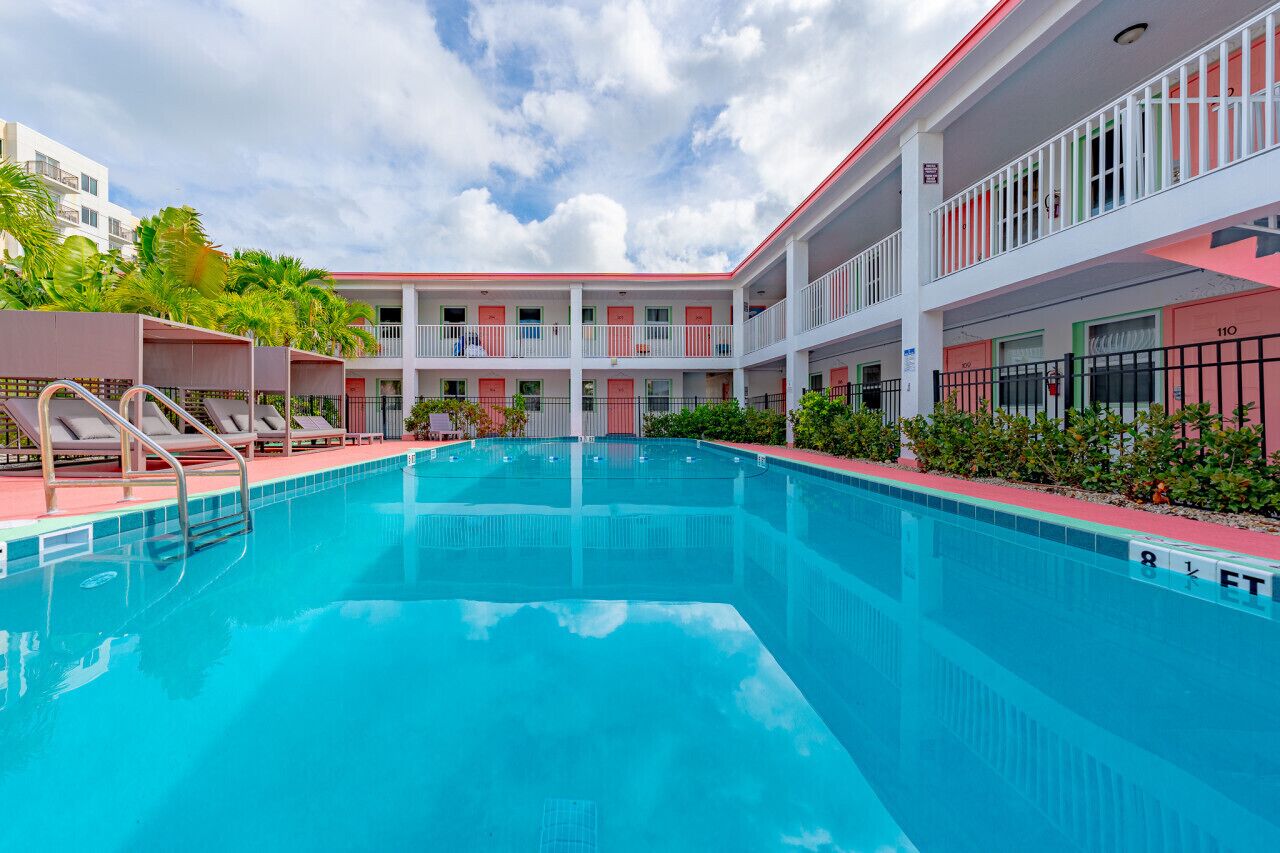 A swimming pool with lounge chairs and a multi-story building with balconies.