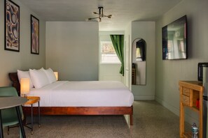 Ein Hotelzimmer mit Bett, Schreibtisch, Sessel, Fernseher und Spiegel.