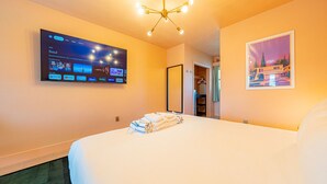 A hotel room with a large bed, a flat-screen TV mounted on the wall displaying a streaming service interface, a framed picture on the wall, and a neatly folded towel on the bed.
