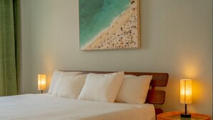 Una habitación de hotel con una cama, dos lámparas de noche, un cuadro de una playa y una cortina verde.