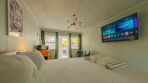 Habitación de hotel con una cama grande, un escritorio con silla, un televisor en la pared mostrando varios canales y vista al exterior a través de una puerta.