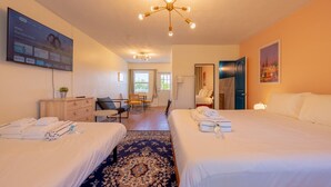 A hotel room with two beds, a desk, a chair, a television, and a chandelier. - 2203 · 3 Min Walk -> Beach / Heated Pool / Free Parking (Clearwater)