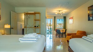 Une chambre d’hôtel avec deux lits, un coin salon avec une table et des chaises, une étagère en bois et une vue sur l’extérieur.