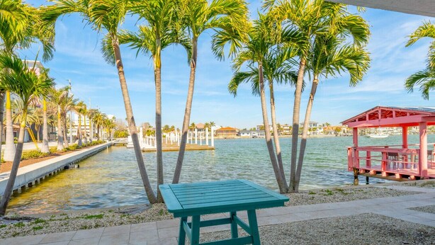 Une vue sur le bord de l’eau, avec des palmiers, un quai et un kiosque rouge.
