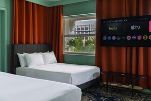 Habitación de hotel con dos camas, un televisor mostrando Hulu y Apple TV, y una ventana con vista a un edificio y palmeras.