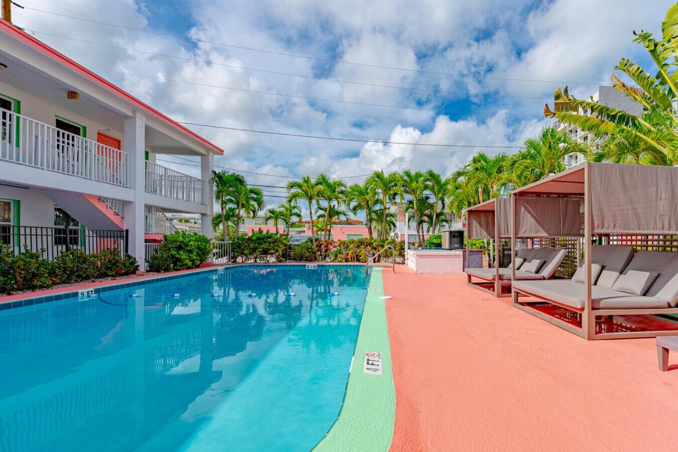 A swimming pool with a red and green border, surrounded by palm trees and a building with balconies.