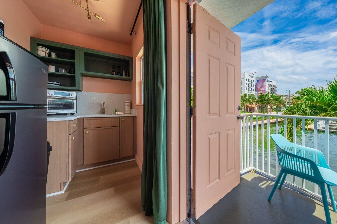 Una cocina con horno integrado, refrigerador y ventana con vista a un balcón que tiene una silla.