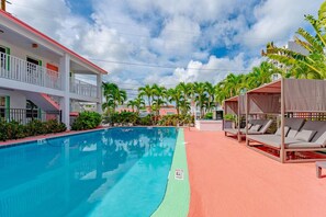 A swimming pool with a red and green border, surrounded by palm trees and a building with balconies.