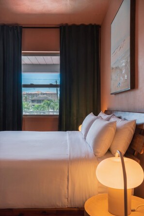 A hotel room with a bed, a nightstand, a lamp, and a window with curtains. - Bay View Studio with Two Beds and Balcony (Clearwater)