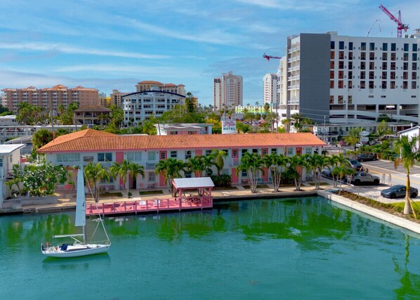 A marina with a sailboat, a building with a red roof, and a hotel in the background.
