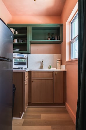 A compact kitchen with wooden cabinets, a built-in oven, and a window with curtains. - 2204 · 3 Min Walk -> Beach / Heated Pool / Free Parking (Clearwater)