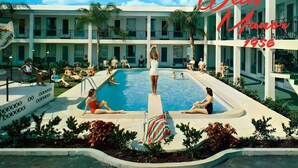A hotel pool area with multiple swimming pools, palm trees, and people relaxing.