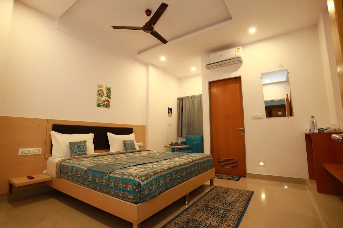 A bedroom with a bed, bedside table, nightstand, ceiling fan, air conditioning unit, and a mirror.