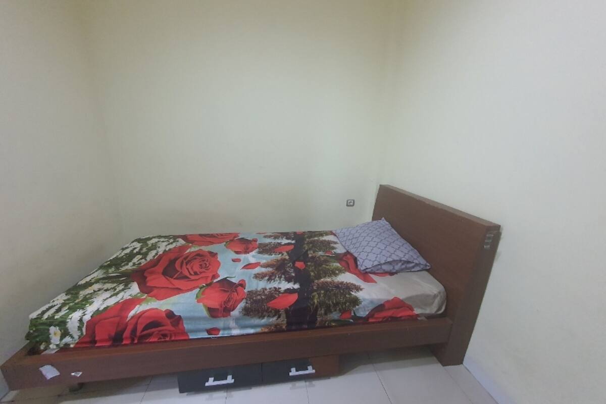 Una cama individual con una colcha estampada, cabecera de madera y un cajón pequeño debajo.