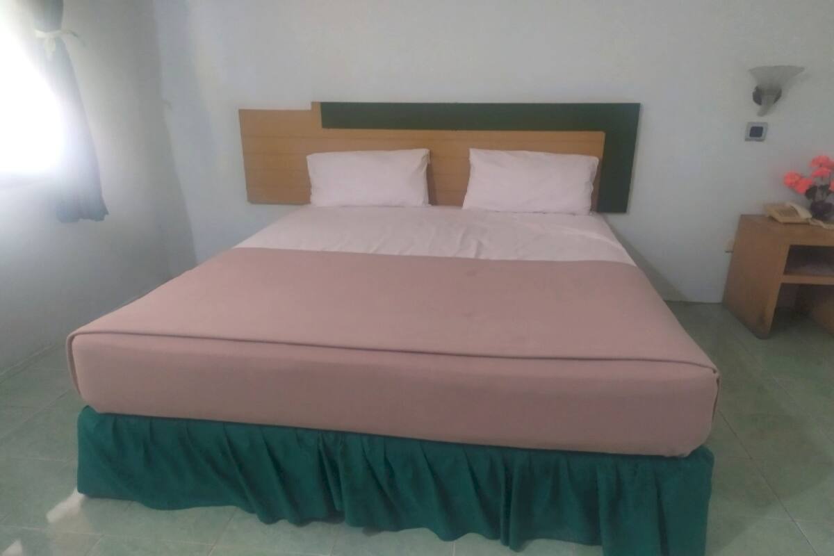 Una cama bien hecha con cabecera de madera y falda verde al pie.