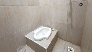 A small, tiled bathroom with a white toilet, a shower drain, and a visible pipe. - OYO 3243 3 Be Garden Hotel (Penajam)