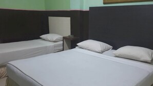 A room with two single beds, each with white linens and pillows. There is a small table between the beds with a lamp on it. The walls are painted in two colors, green and black. - OYO 3243 3 Be Garden Hotel (Penajam)
