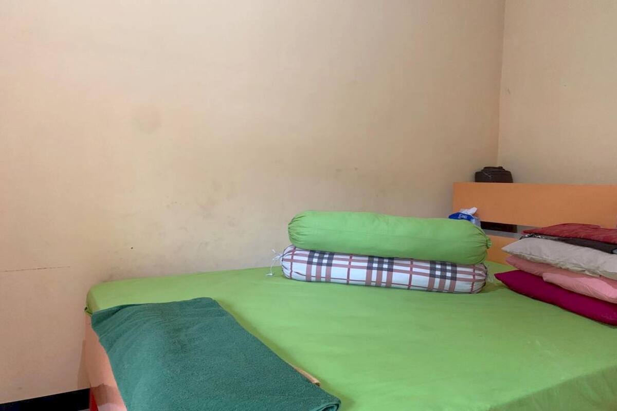 Una habitación pequeña y sencilla con una cama individual, una colcha verde y algunos almohadones.